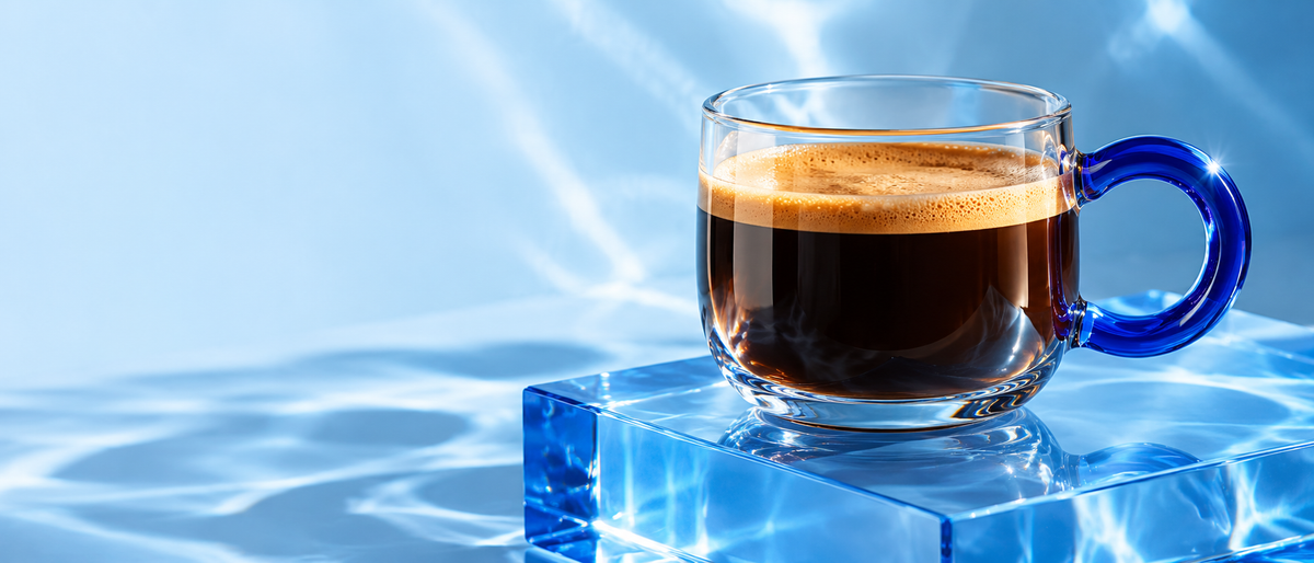 Clear glass espresso cup with cobalt handle on an icy blue plinth